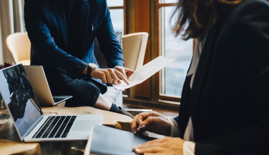 Woman working on a laptop and checking documents a man showing to her