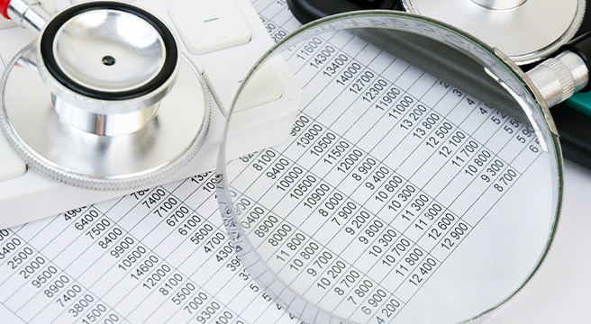 Photo: a stethoscope, spreadsheet, and magnifying glass, symbolizing healthcare, data analysis, and investigation in the context of detecting fraud, waste, and abuse in New Jersey Medicaid