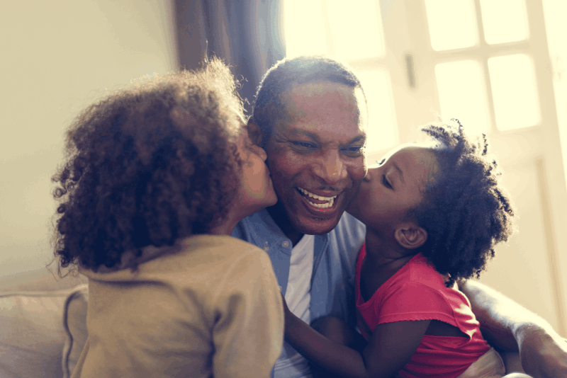 Father being kissed  by 2 young daughters