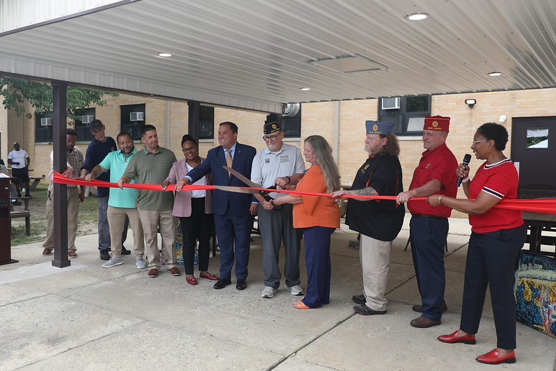 Commissioner Vincent Solomeno, Deputy Commissioner Esther Chucharalao, Superintendent Tori Hill, members of the New Jersey State American Legion, and Veterans Haven South residents about to cut the ceremonial red ribbon with giant scissors.