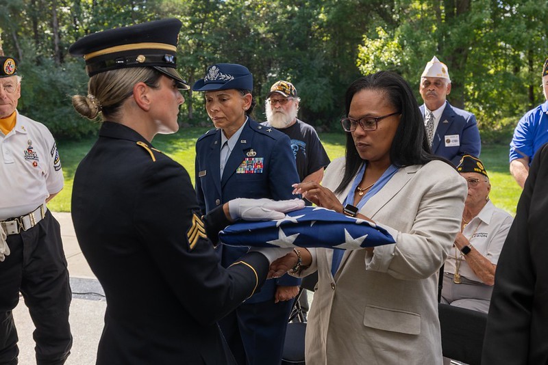 Deputy Commissioner Esther Chucaralao receiving folded American flag during ceremony.