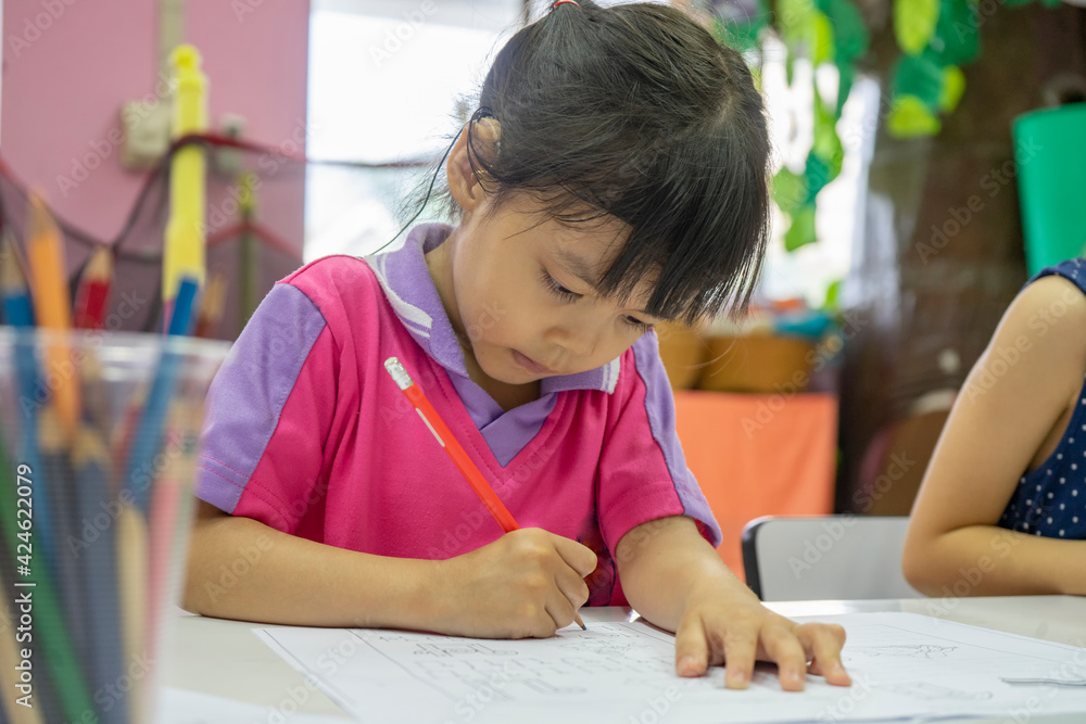 elementary student writing while sitting at a desk wearing a hearing aid