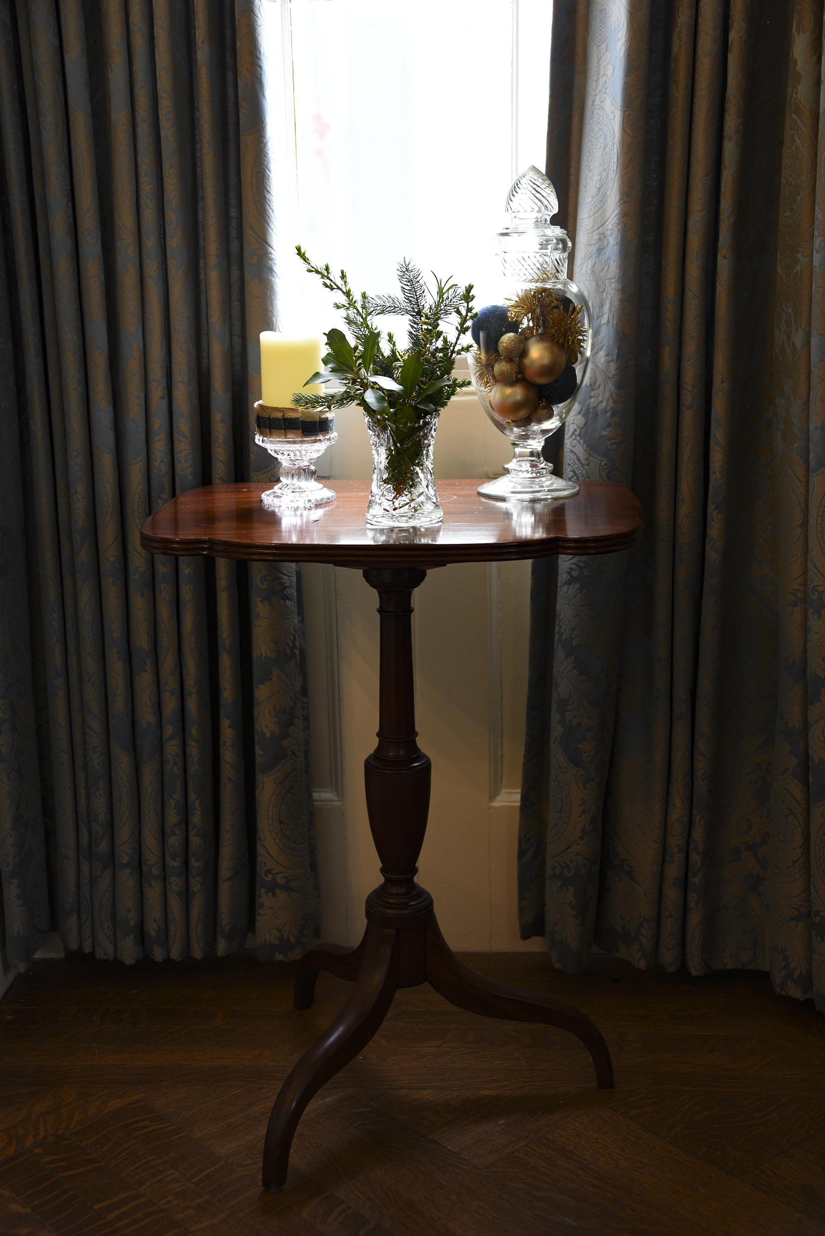 A side table in a Parlor window shines with gold and greens and glass decor.