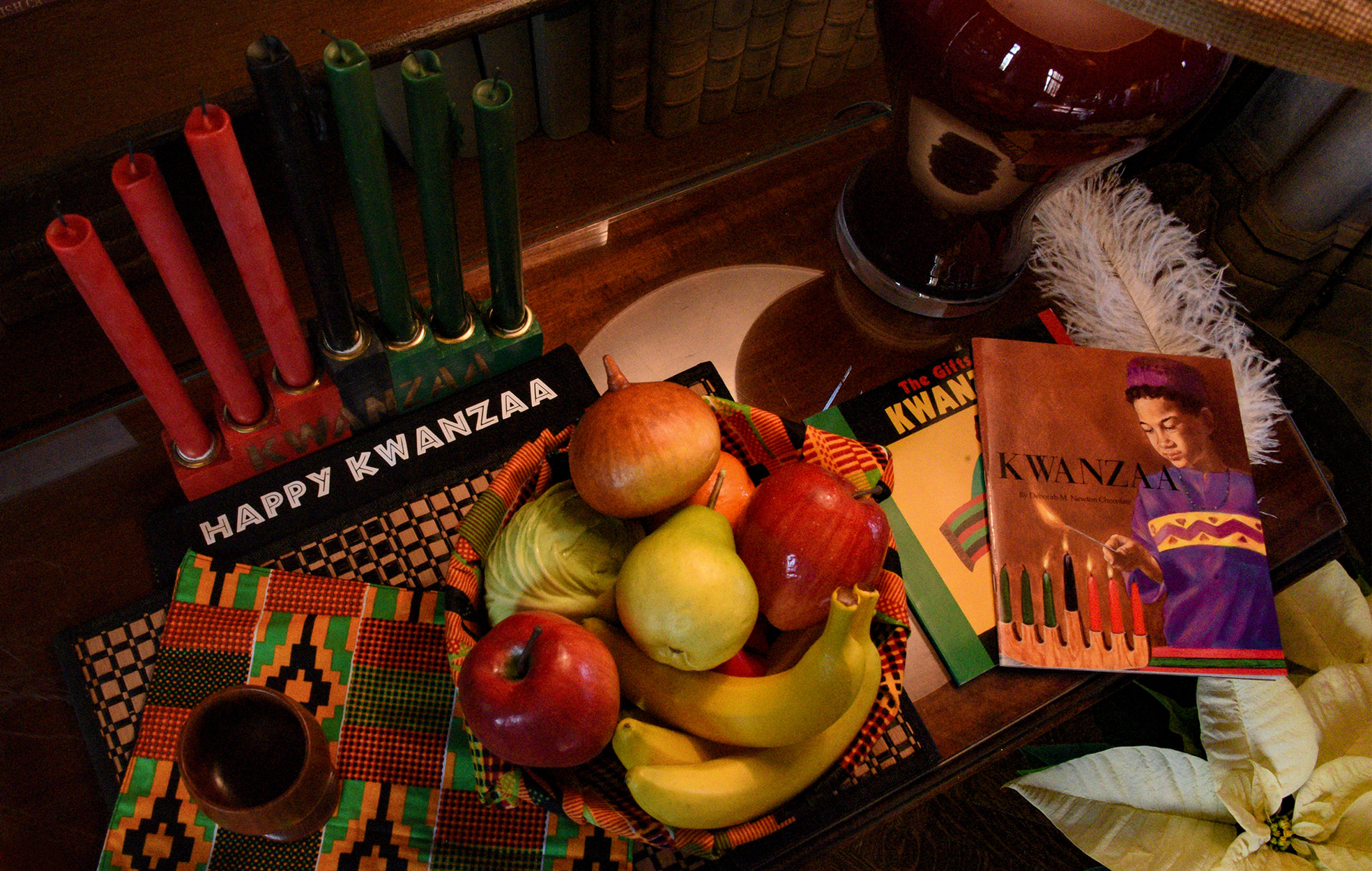 In the Library, a close view of a Kwanzaa display including fruit, traditional candles, books and a single feather.