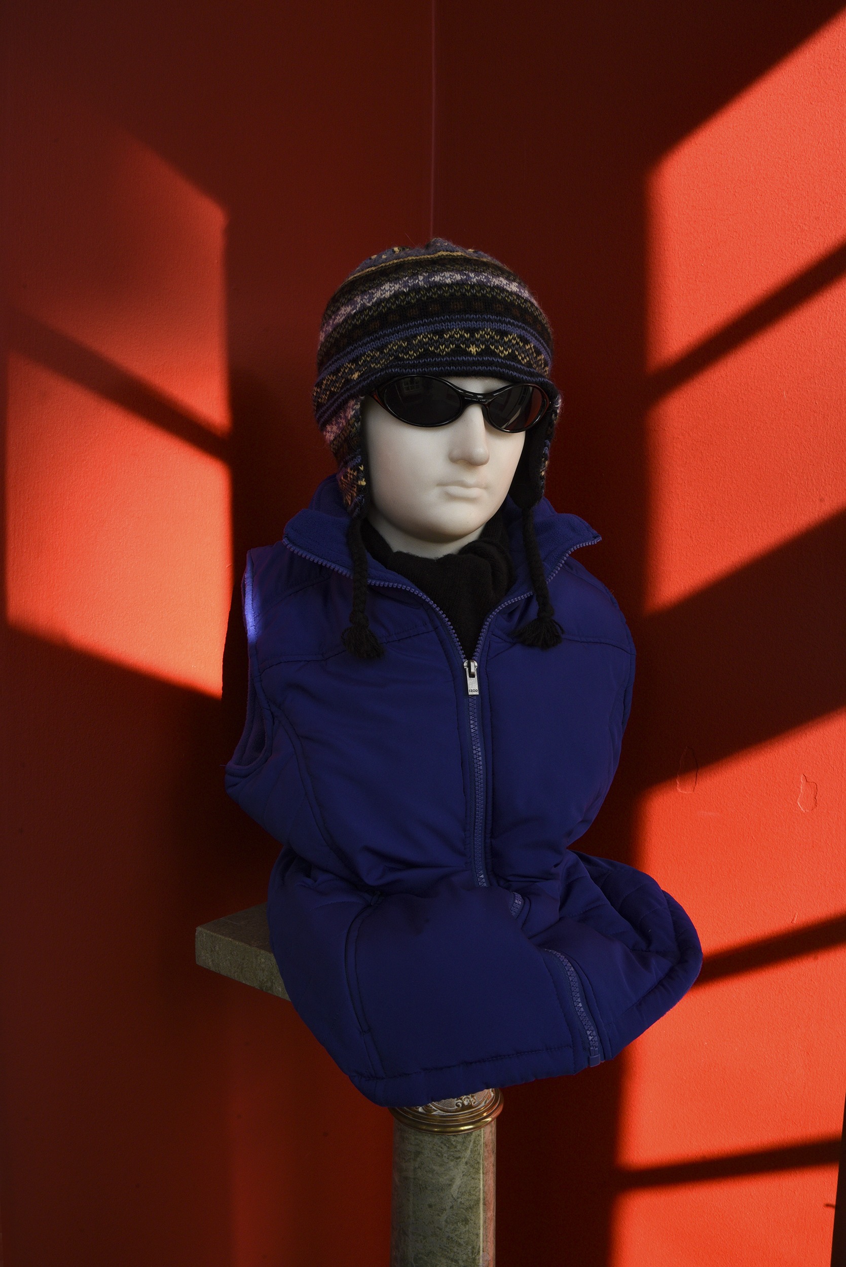 Just outside the Governors Study, a bust of a young man is whimsically dressed in ski gear and sunglasses. Geometric patches of sunlight on crimson walls frames the figure.