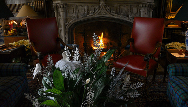 photo - A cozy fire framed by leather chairs in the Library with a centerpiece of white orchids and peace lilies in the foreground. Library Decor by the Allentown Garden Club.