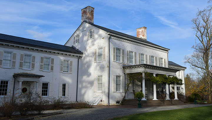 photo - Bright blue sky and exterior photo of Morven, New Jerseys first Governors residence. White painted brick mansion with front portico, greenery wraps four columns.