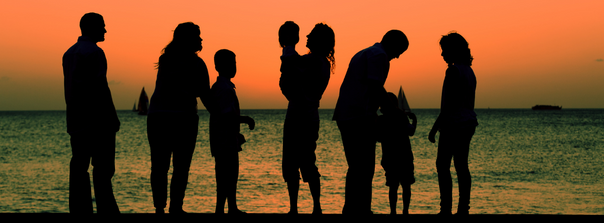 Five adults and three children on a beach during a sunset.