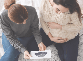 Pregnant person and their friend looking at an ultrasound image.