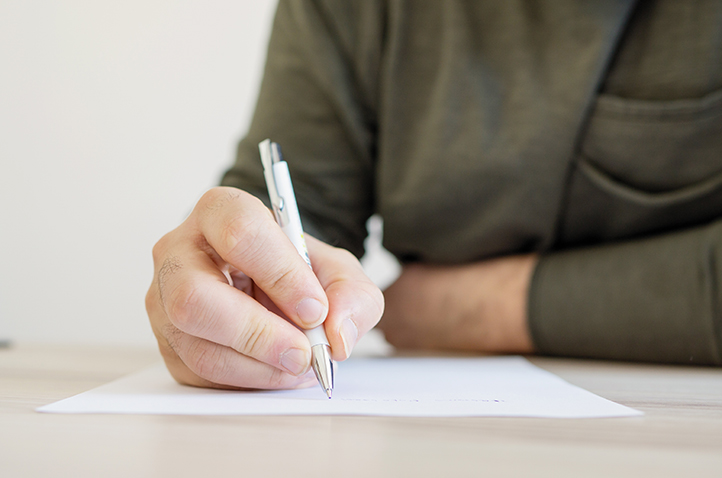 A man holding a pen and writing something on a sheet of paper.