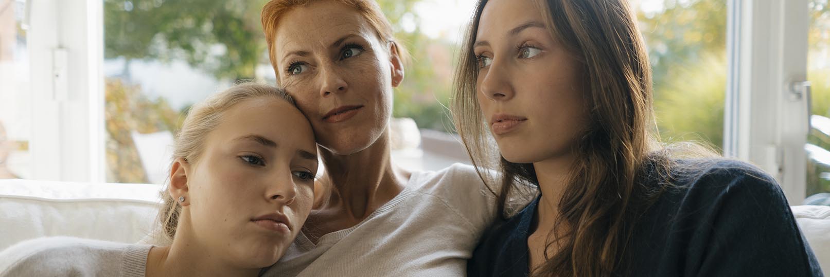 woman looking somber with her daughters, sitting on a couch