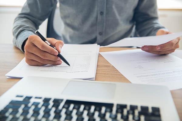 person on laptop with paperwork on table