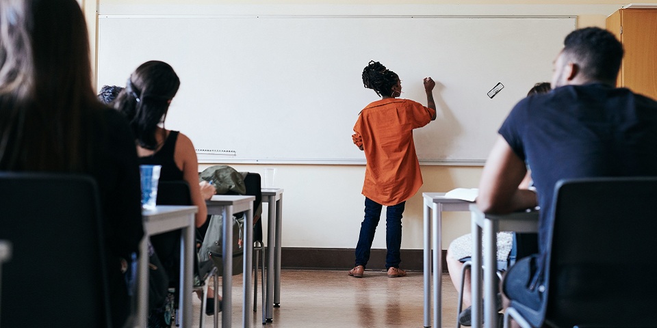 a classroom of adult learners and their teacher who is facing a whiteboard