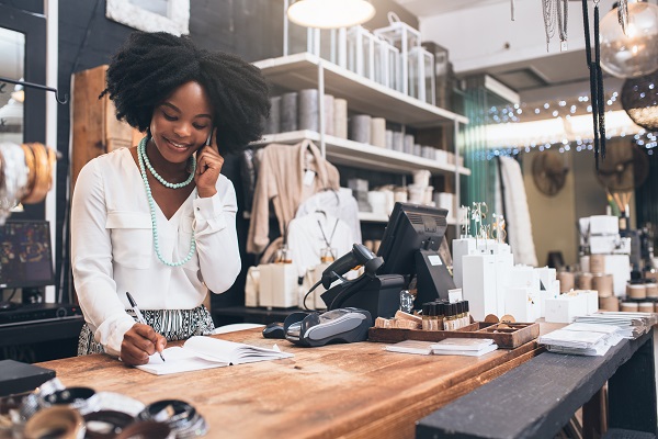 Woman using her cellphone while standing behind the counter in her shop