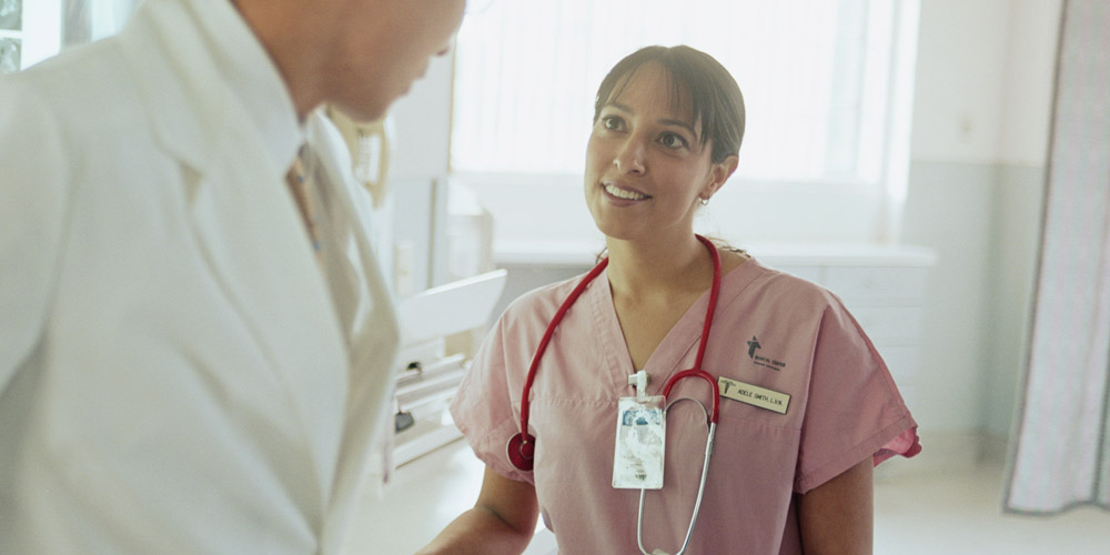 A female nurse or doctor talking to a doctor in a hospital setting.
