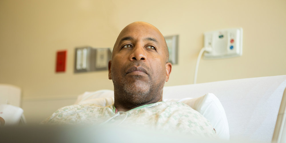 A man sitting up in a hospital bed, looking thoughtful