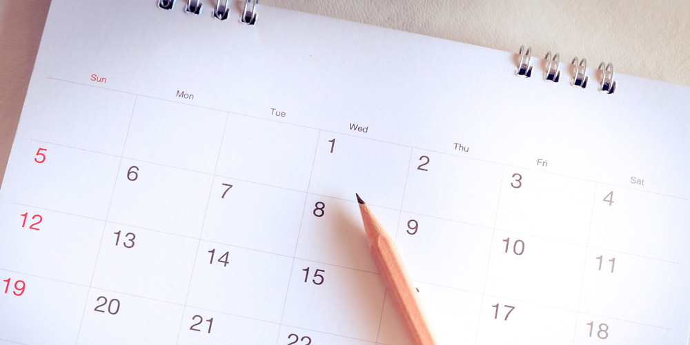 A close-up of a month page in a desk calendar with a sharpened pencil lying on top of it