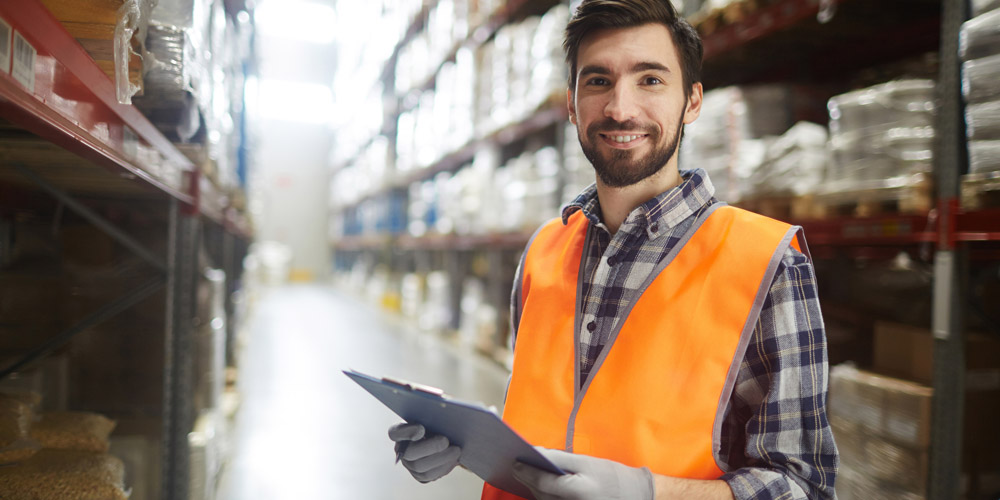A warehouse supervisor standing with a clipboard in hand, smiling