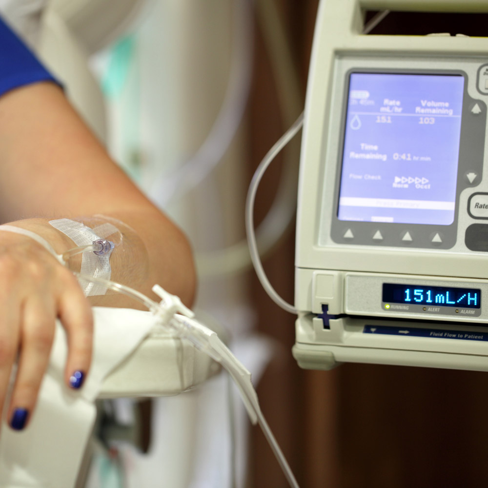 A closeup of a woman's arm with an IV in it; she's sitting in a chair in a hospital next to the IV pump