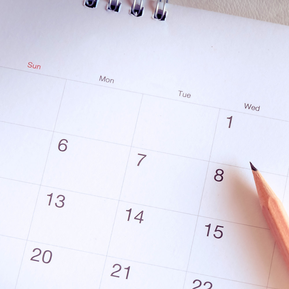 a desk calendar opened to a month page view, with a sharpened pencil lying on top