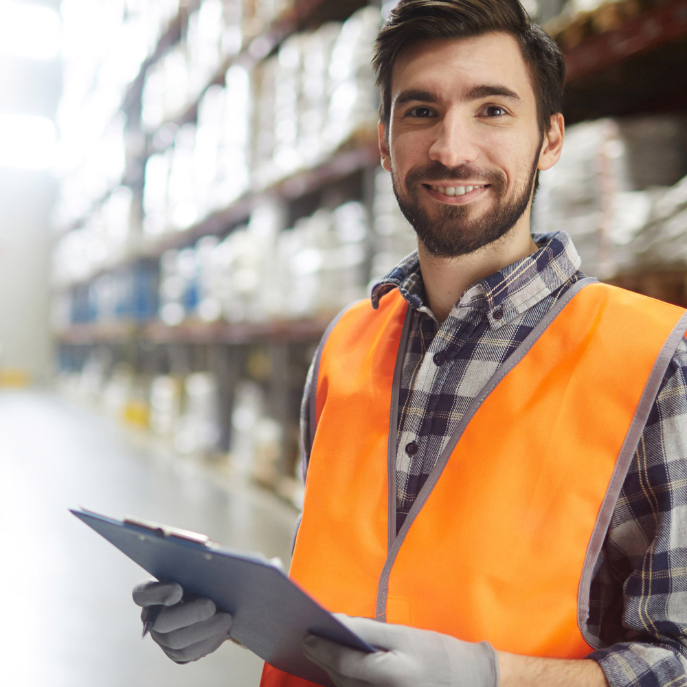 A warehouse supervisor standing with a clipboard in hand, smiling