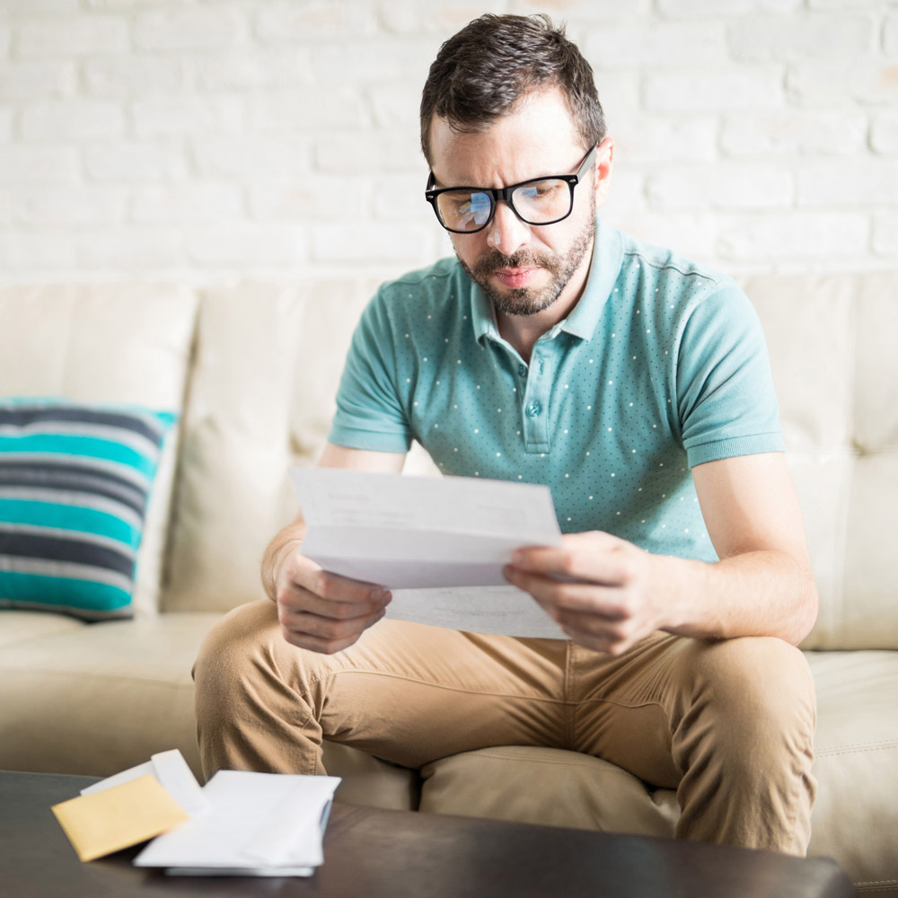 A man on a sofa opening mail and looking confused