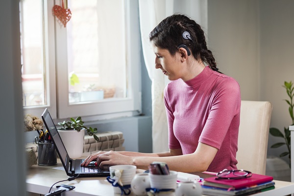 Young woman with hearing device working at laptop