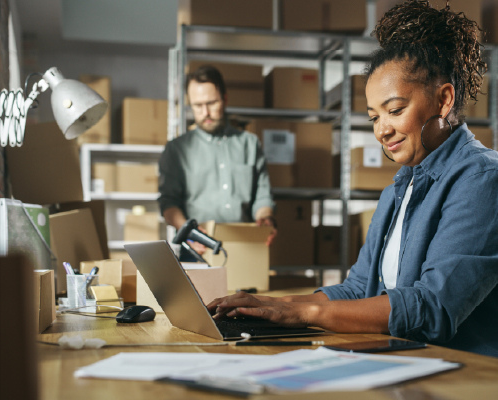 Woman working at a computer and a man packing boxes