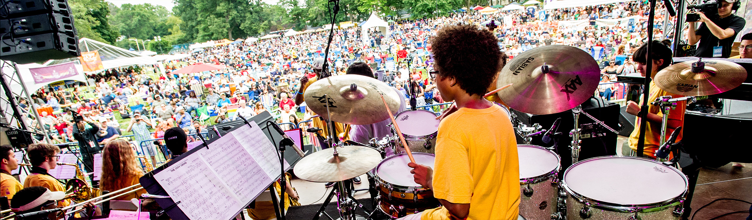 kids performing as a band on an outdoor stage to a large audience