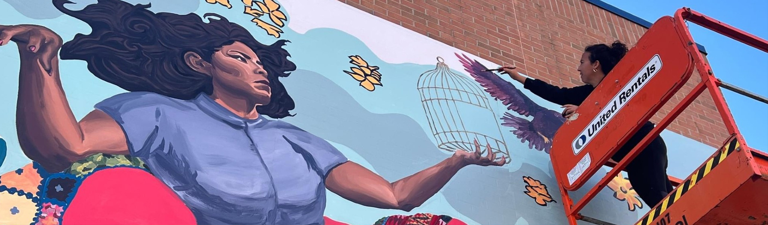 an artist painting a large outdoor mural on a brick wall