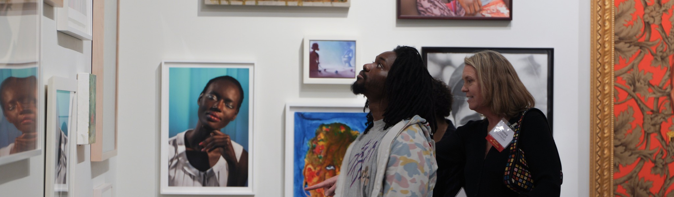 Person standing looking at artwork in a museum with two people behind them talking.