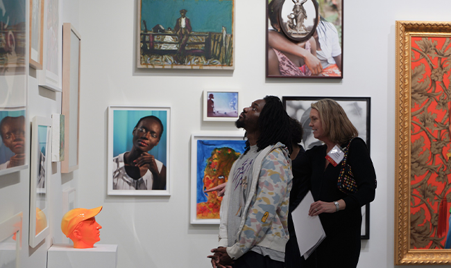 Person standing looking at artwork in a museum with two people behind them talking