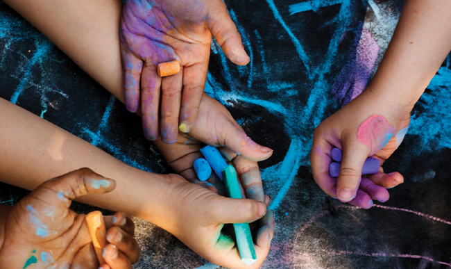 children’s hands drawing and holding chalk against on pavement