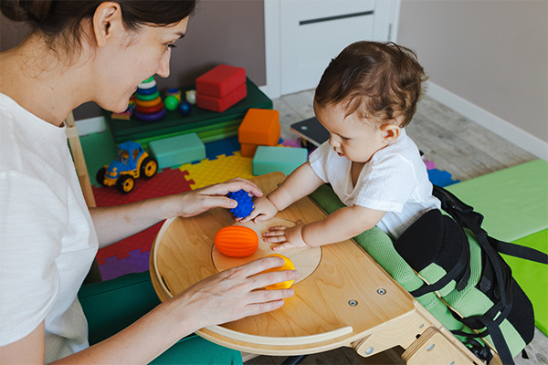 Early intervention practitioner and the child are in a therapy room with gray and white walls